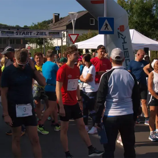Marathonteilnehmer versammeln sich an der Startlinie. Sie tragen verschiedene Laufausrüstungen und nummerierte Startnummern. Eine Person mit der Startnummer 7 ist im Vordergrund.