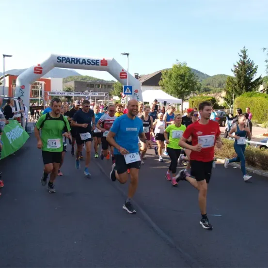 Eine Gruppe von Läufern nimmt an einem Marathon teil. Sie tragen Nummern auf ihren Trikots. Hinter ihnen ist ein Banner mit dem Wort Sparkasse.