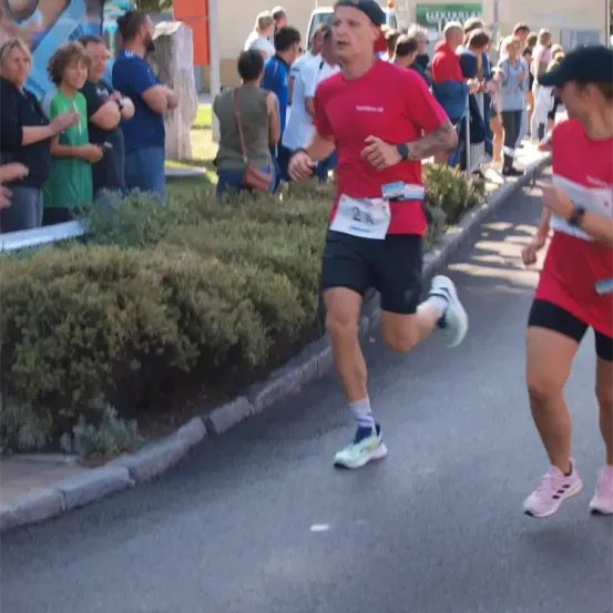 Läufer bei einem Marathonrennen mit Zuschauern am Straßenrand, ein Läufer trägt ein rotes Shirt mit der Nummer 24.