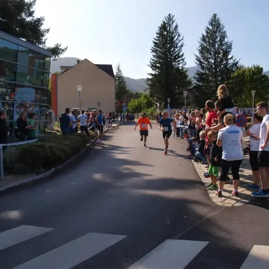 Marathonläufer sprinten eine Straße hinunter, während Zuschauer vom Bürgersteig zusehen. Die Läufer befinden sich in der Mitte der Straße, mit einem Gebäude und Bäumen an der Seite.