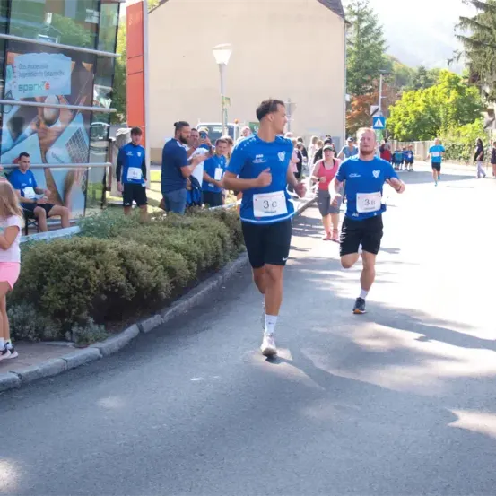 Eine Gruppe von Läufern nimmt an einem Marathon teil. Sie laufen auf der Straße, während einige Zuschauer von der Seite zusehen.