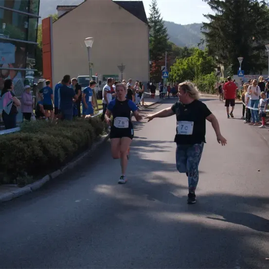 Zwei Läufer nehmen an einem Marathon teil, einer trägt ein blaues Shirt und der andere ein schwarzes. Zuschauer stehen am Straßenrand.