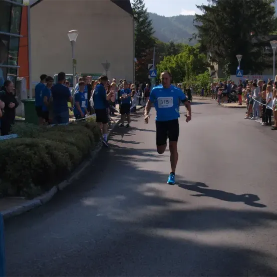 Ein Marathonläufer mit der Nummer 315 auf dem Shirt läuft die Straße hinunter, während die Zuschauer ihn anfeuern.