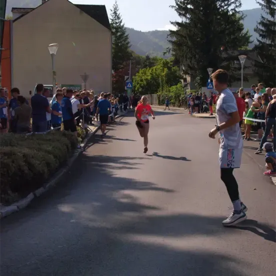 Ein Marathonläufer sprintet eine Straße hinunter, mit Zuschauern an den Seiten, Bergen im Hintergrund und Straßenlaternen und Gebäuden in der Nähe.