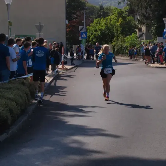 Eine Marathonläuferin mit der Nummer 577 auf dem Trikot läuft in der Mitte der Straße, während mehrere Leute stehen und zuschauen.