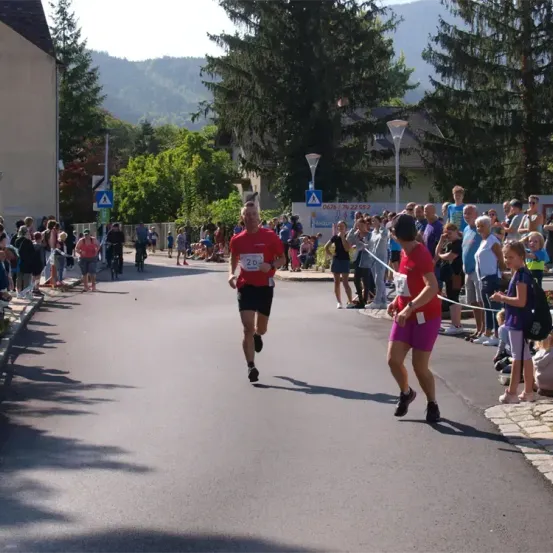 Ein Marathonläufer mit der Nummer 20 läuft auf der Straße, während eine Menge Menschen zusieht. Einige von ihnen halten Kameras.
