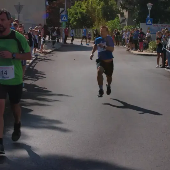 Ein Läufer befindet sich mitten in einem Marathon. Zuschauer jubeln von der Seite. Der Läufer trägt ein blaues Shirt.