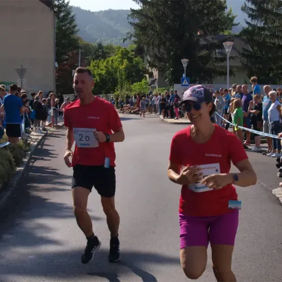 Ein Mann und eine Frau laufen bei einem Marathon. Der Mann hat die Nummer 2D auf seinem Shirt. Die Frau lächelt und trägt eine Kappe.