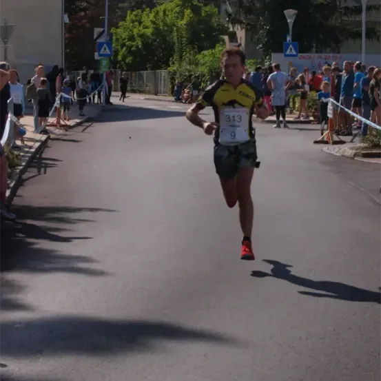 Ein Marathonläufer mit einem Trikot, das die Nummer 313 trägt, läuft die Straße hinunter, während Zuschauer auf dem Bürgersteig zusehen.