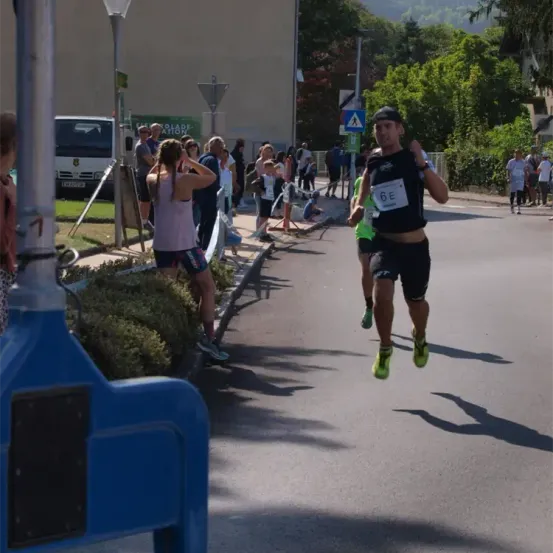 Ein Läufer mit der Nummer 6E auf dem Trikot läuft einen Marathon, mehrere Menschen beobachten ihn von der Seite.