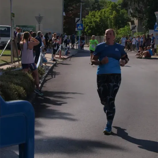 Eine Frau läuft während eines Marathons auf der Straße, umgeben von Zuschauern und Bäumen. Ein anderer Läufer folgt ihr.