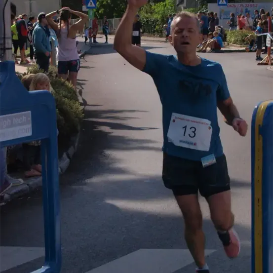 Ein Mann mit einem blauen Shirt und der Nummer 13 läuft einen Marathon, während eine Menge Leute am Straßenrand zuschaut.