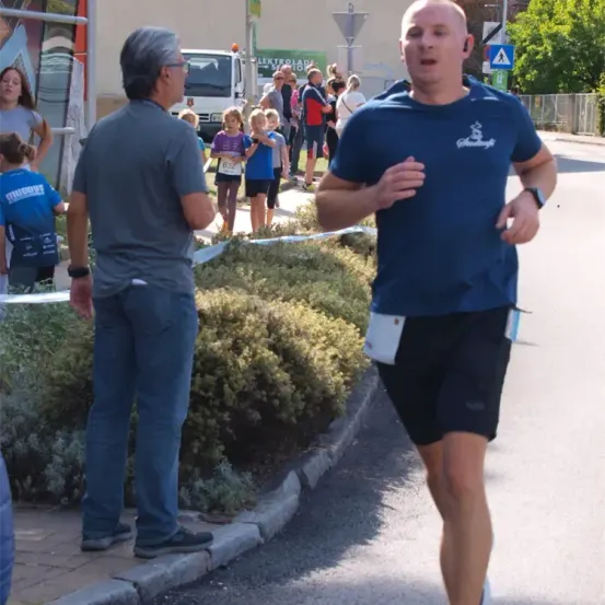 Ein Mann läuft auf der Straße, während Zuschauer und ein Pickup-Truck im Hintergrund sind. Eine Person schaut ihn an, während er läuft.