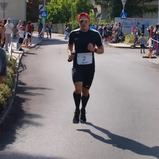 Ein Läufer mit Sonnenbrille und rotem Hut läuft eine Straße hinunter, an der eine Menschenmenge auf dem Bürgersteig steht.