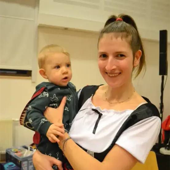 Eine Frau in einem schwarzen und weißen Kleid hält ein Baby in den Armen. Sie lächeln beide für ein Foto.