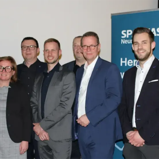 Eine Gruppe von Fachleuten steht in einer Reihe, lächelt und posiert für ein Foto. Sie sind in formeller Kleidung gekleidet.