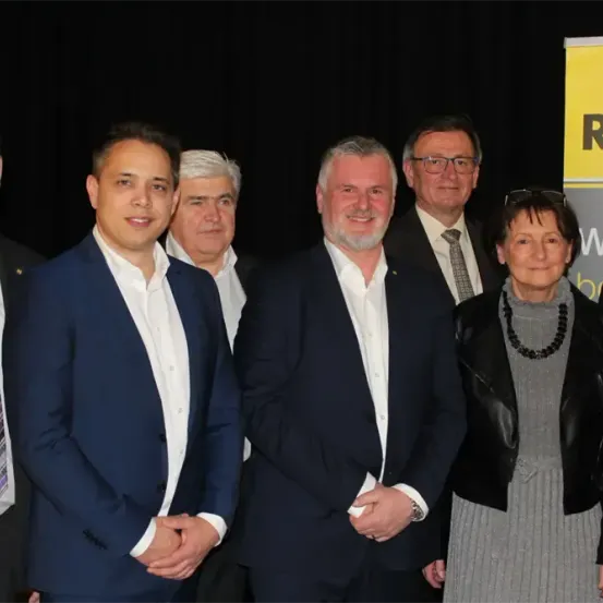 Eine Gruppe von Männern und einer Frau steht zusammen, wahrscheinlich für ein Foto. Sie sind in formeller Kleidung gekleidet.