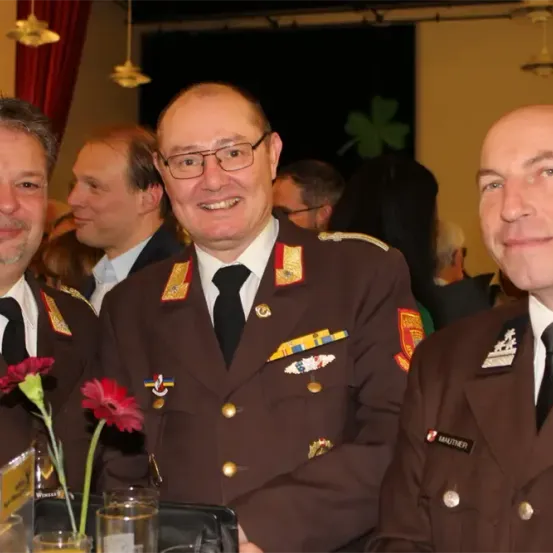Drei Männer in Militäruniformen posieren für ein Foto mit einer roten Blume auf dem Tisch.