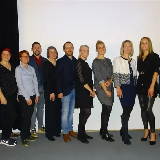 Eine Gruppe von Menschen, wahrscheinlich Kollegen, steht für ein Foto zusammen. Sie tragen formelle Kleidung.