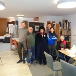 Eine Gruppe von Menschen posiert für ein Foto in einem Raum. Eine Frau hält eine Medaille. Ein Tisch steht vor ihnen.