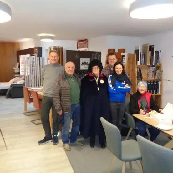 Eine Gruppe von Menschen posiert für ein Foto in einem Raum. Eine Frau hält eine Medaille. Ein Tisch steht vor ihnen.