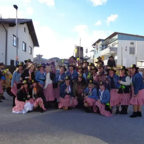 Eine Gruppe von Frauen in Cowboy-Hüten und rosa Kleidern posiert für ein Foto vor Gebäuden.