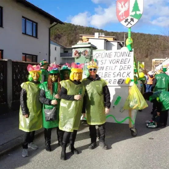 Eine Gruppe von Menschen in grünen Kostümen steht vor einem Schild mit der Aufschrift Grüne Tonne. Sie nehmen wahrscheinlich an einer Parade teil.