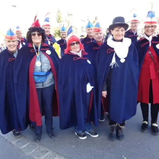 Eine Gruppe von Menschen in traditionellen Kostümen steht gemeinsam auf der Straße und lächelt für ein Foto. Sie tragen blaue Umhänge und verschiedene Hüte.