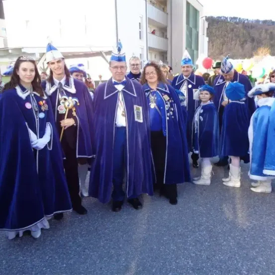 Eine Gruppe von Menschen in blauen Kostümen, Hüten und Stiefeln posiert für ein Foto im Freien, mit Gebäuden und Bergen im Hintergrund.