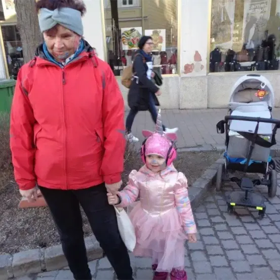 Eine erwachsene Frau mit blauer Farbe im Gesicht hält die Hand eines kleinen Mädchens in einem rosa Kostüm auf der Straße.