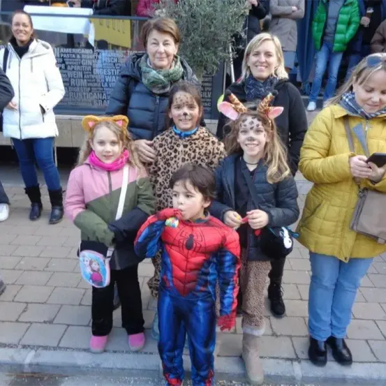 Eine Gruppe von Kindern und Erwachsenen steht auf einem gepflasterten Bürgersteig, wahrscheinlich bei einer Kostümparty. Sie alle lächeln. Ein Junge in einem Spider-Man-Kostüm hält eine Süßigkeit.