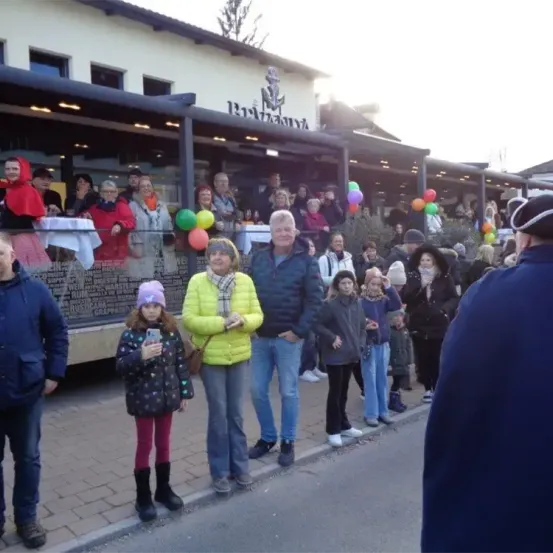 Eine Gruppe von Menschen steht vor einem Restaurant namens "Brigantina". Einige halten Luftballons. Ein Mädchen macht ein Foto mit ihrem Handy.