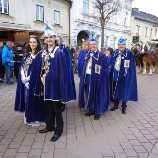Eine Gruppe von Menschen in blauen Umhängen und Mützen steht vor einem Gebäude mit einer Pferdekutsche in der Nähe.