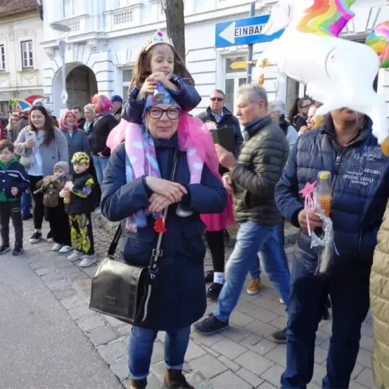 Eine Frau trägt ein Kind auf der Schulter in einer Menschenmenge. Das Kind hat eine Krone und einen Ballon im Hintergrund.