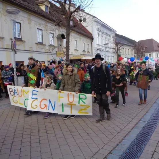 Eine Gruppe von Menschen zieht in einem Umzug und hält ein Schild, das Baume fur Gloggnitz liest.
