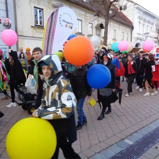 Eine große Menschenmenge zieht in Kostümen und mit verschiedenfarbigen Luftballons durch die Straße.