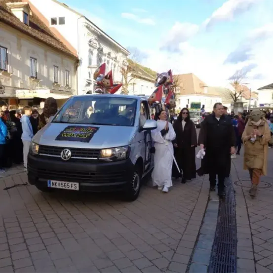 Ein mit Ballondekorationen verzierter Star Wars-Themen-Van steht auf einer Straße, mit Leuten in Kostümen, die darum herumlaufen.