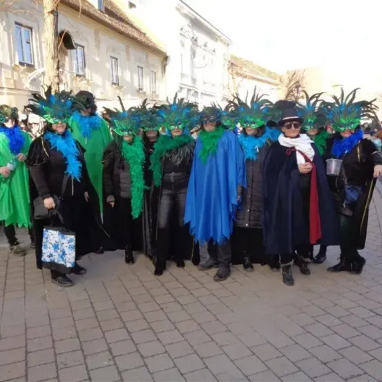 Eine Gruppe von Menschen in leuchtenden Kostümen und Masken steht auf einem Stadtplatz, wahrscheinlich für ein Festival.