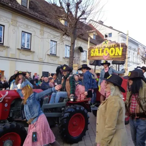 Ein Umzug mit Menschen in Western-Kostümen auf einem Traktor vor einem Gebäude mit dem Schild Old West Saloon.