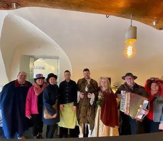 Eine Gruppe von Menschen in historischen Kostümen posiert für ein Foto in einem Raum mit gewölbten Decken und einer Vintage-Leuchte.