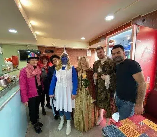 Eine Gruppe von Menschen in Kostümen steht in einem Essbereich, mit einem Tresen und einem Kühlschrank dahinter.