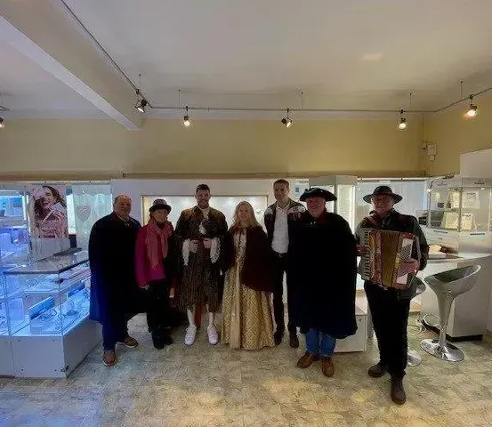 Eine Gruppe von Menschen in mittelalterlicher Kleidung posiert für ein Foto in einem Geschäft mit Vitrine und Stühlen.