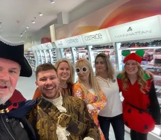 Eine Gruppe von Menschen in Kostümen, darunter ein Pirat, eine Marienkäferin und andere, lächeln in einem Geschäft mit einer Catrice-Kosmetik-Ausstellung.