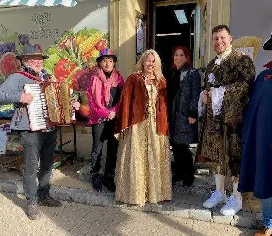 Eine Gruppe von Menschen in verschiedenen Kostümen posiert vor einem Geschäft, wobei ein Mann Akkordeon spielt.
