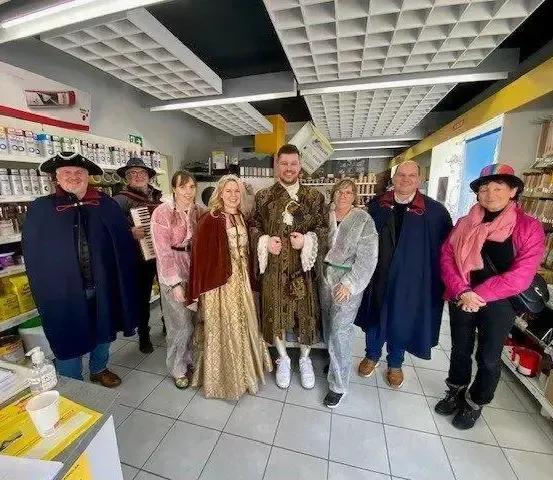 Eine Gruppe von Menschen in historischen Kostümen posiert für ein Foto in einem Geschäft. Sie stehen in einer Reihe mit Regalen voller Produkte im Hintergrund.