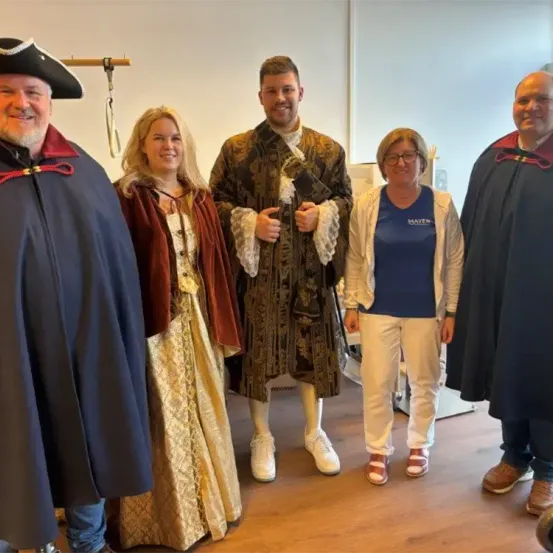 Fünf Menschen in Kostümen stehen auf einem Holzboden. Einer trägt einen Piratenhut, ein anderer ein blaues T-Shirt, und drei andere tragen lange Roben. Sie scheinen für ein Foto zu posieren.