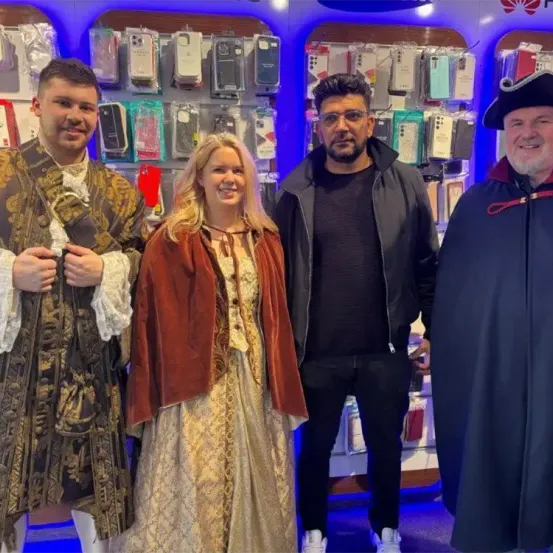 Vier Personen posieren für ein Foto vor einem Geschäft mit ausgestellten Handyhüllen. Die Leute sind in Kostümen gekleidet, und der Mann auf der rechten Seite trägt einen Piratenhut.