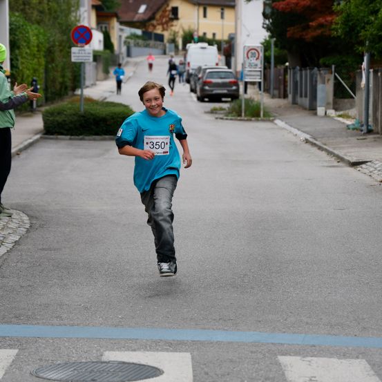 Ein junger Junge mit einem blauen Shirt und der Nummer 350 läuft auf der Straße, wahrscheinlich bei einem Marathon.
