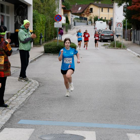 Ein Mädchen mit der Nummer 339 läuft in einem Marathon. Zuschauer feuern sie von der Straßenseite an.
