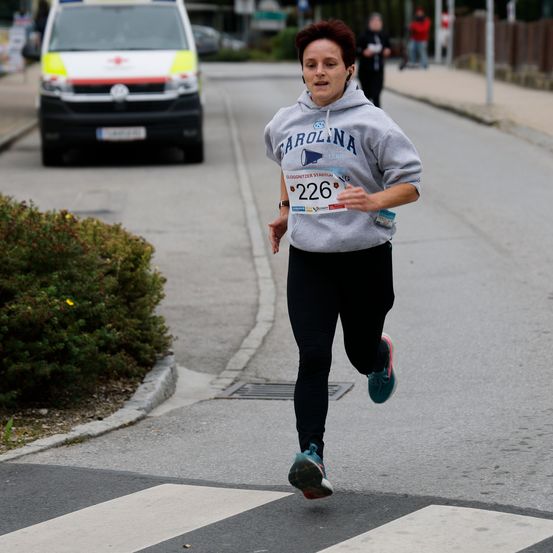Eine Frau mit einer grauen Kapuzenjacke mit Carolina und der Nummer 226 läuft auf der Straße, während ein Krankenwagen hinter ihr fährt.